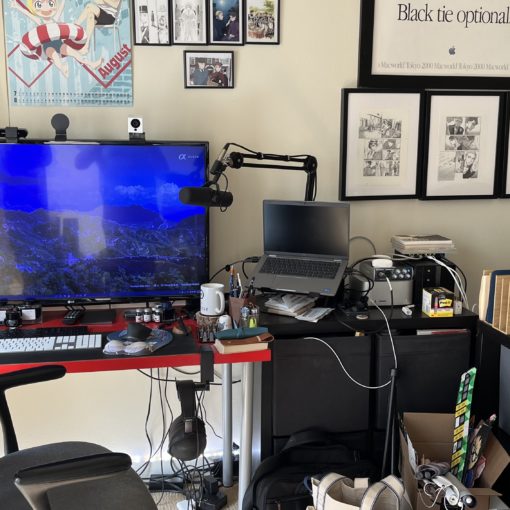 Photo of a work from home desk. The main workspace is a red table on the far left. To its right sits an IKEA KALLAX with computers on top of it. Forming an L-shape to its right is another IKEA KALLAX with the top mostly empty.