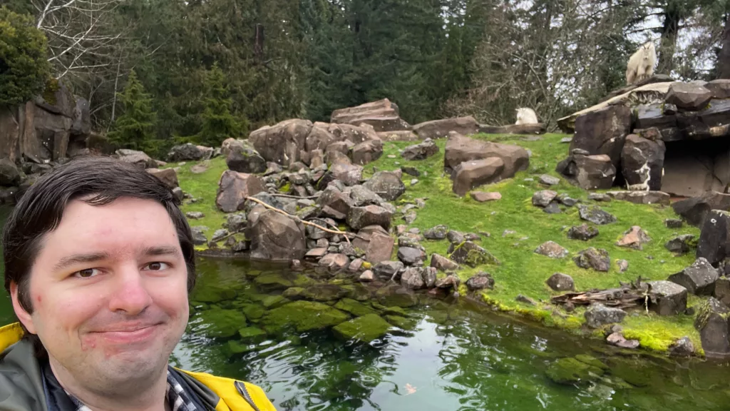 Selfie taken in front of the mountain goats exhibit at the Oregon Zoo as two goats look on.
