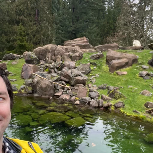 Selfie taken in front of the mountain goats exhibit at the Oregon Zoo as two goats look on.