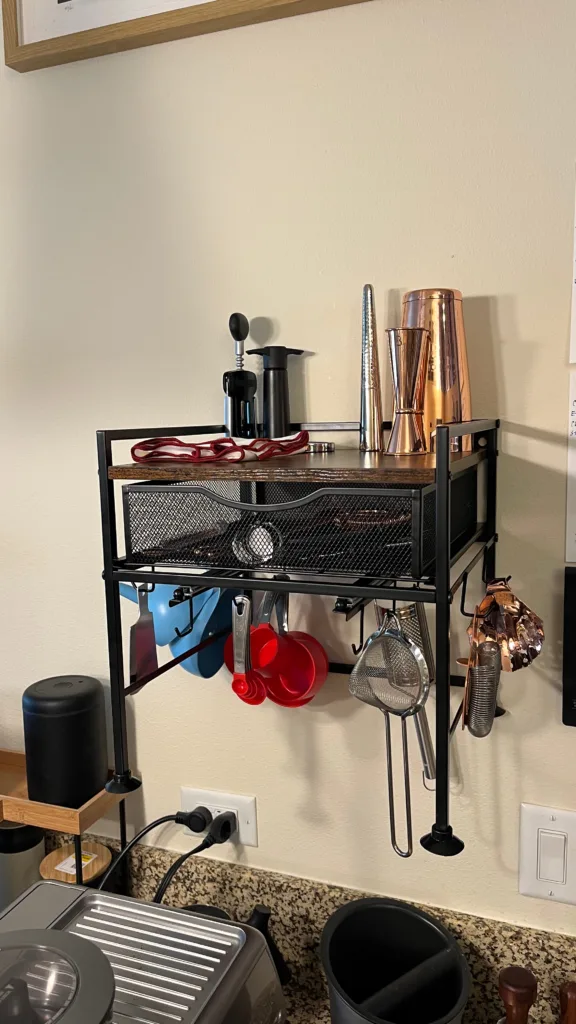 Photo of the front and top of a kitchen organizer mounted to a wall above an espresso machine.