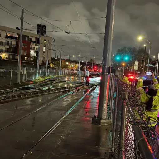 Photo of a car high centered in a TriMet MAX switch near NW Hoyt and NW 3rd. Several TriMet employees assess the situation as Portland Police responds to the scene.