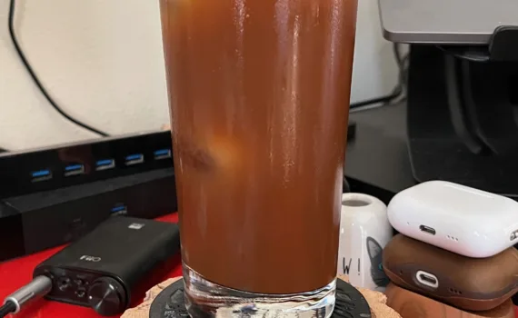 Photo of a glass of espresso tonic on a coaster on a desk.